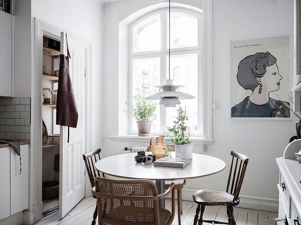 hình ảnh toàn cảnh phòng ăn phong cách Bắc Âu đơn giản với bàn tròn, tranh treo tường, chậu cây xanh đặt ở bệ cửa sổ kính